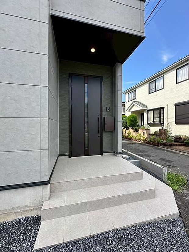 モダンなデザインの玄関が目を引きます。落ち着いた色合いの外壁とシンプルな玄関ドアが調和しています。玄関前にはゆとりあるスペースが広がり外観がすっきりとした印象です。
