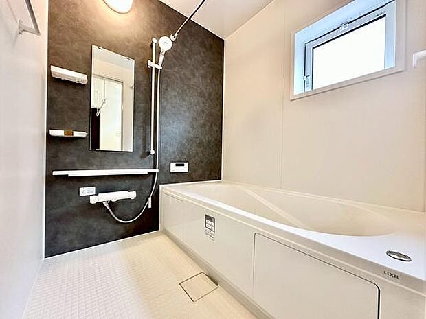 バスルームはシンプルなデザインで清潔感のある印象です。窓が設けられており換気や採光に配慮されています。壁面のアクセントカラーが空間を引き締めています。手すりや鏡収納棚も設置されています。