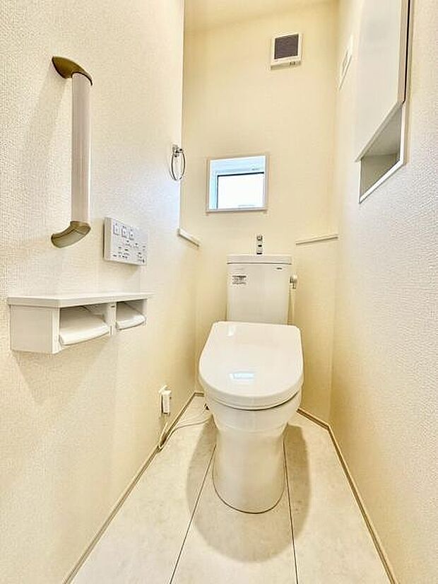 明るい雰囲気のトイレです。手すり付きで使いやすさに配慮されています。壁面収納やペーパーホルダーもすっきりと設置されています。小窓があり換気にも便利です。清潔感のある空間です。