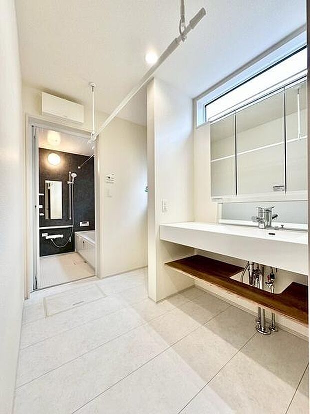 洗面台はシンプルで使いやすいデザインです。大きな鏡が設置されており朝の準備にも便利です。床は明るい色調で清潔感があります。収納スペースも確保されています。浴室へのアクセスもスムーズです。
