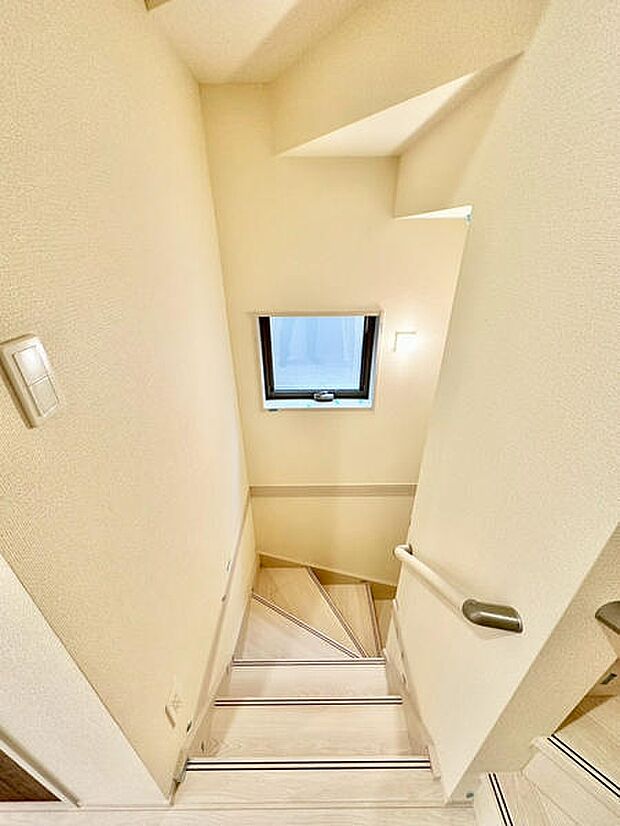 階段部分に設けられた窓から自然光が入り明るい雰囲気です。白を基調とした壁と手すりが清潔感を演出しています。踏み板の形状にも工夫が感じられます。手すりがしっかり取り付けられています。