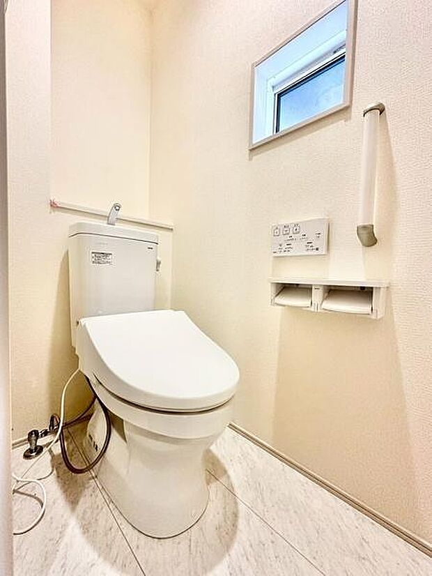 明るい色合いの壁と床が空間を広く見せています。窓付きで換気しやすいトイレです。手すりや操作パネルが設置されており使い勝手にも配慮されています。ペーパーホルダーが2連タイプで便利です。