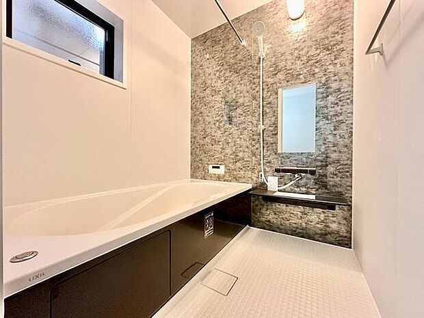 落ち着いた色合いのバスルームで、窓から自然光が入り明るさを感じられます。ゆとりある浴槽でゆったりくつろげ、壁面デザインがアクセントとなった清潔感のある空間です。