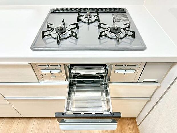 三口コンロ付きで調理の幅が広がります。グリルが備わっていて多用途に対応できます。白を基調とした清潔感あるキッチンです。収納スペースも充実しています。