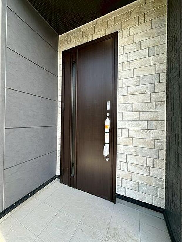 レンガ調の壁が印象的な玄関に、ダークトーンの玄関ドアを組み合わせた落ち着きのあるデザイン。住まいの第一印象を上品に彩ります。