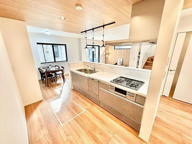 広々とした空間に配置されたキッチンは動線がスムーズで使いやすいデザインです。天井や床のウッド調が温かみを演出しています。ダイニングスペースへの視界が開けており開放感があります。