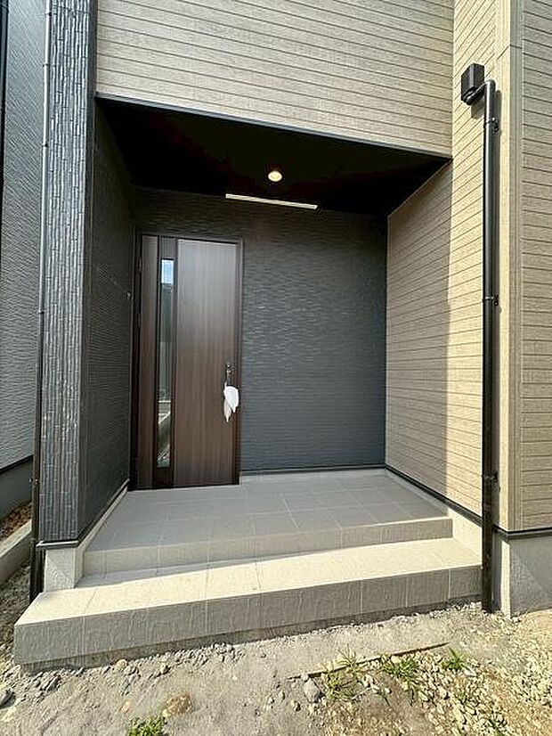 屋根付きの玄関アプローチは、雨の日の出入りもスムーズ。段差を抑えた設計で、毎日の使いやすさにも配慮されています。ダウンライトが足元をやさしく照らし、上質な雰囲気を演出します。