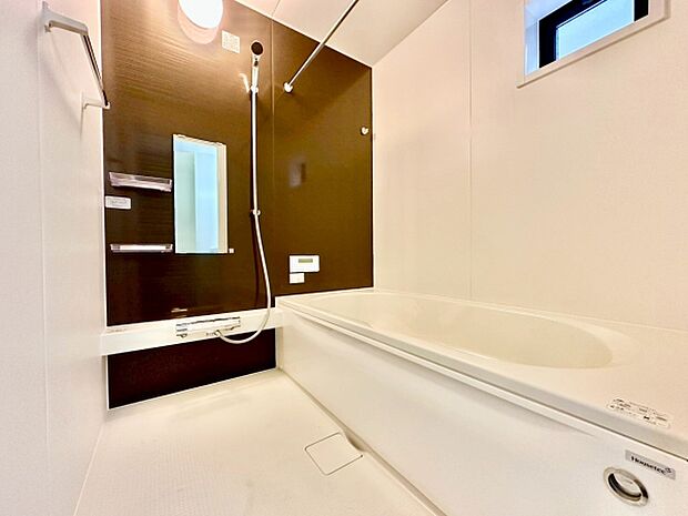 ダークブラウンのアクセントパネルが特徴的なバスルームです。大きめのバスタブと明るい採光窓があり清潔感のある空間です。棚やミラーも設置されており使い勝手に配慮されています。