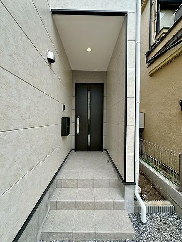 直線的に奥行きを持たせた玄関アプローチは、屋根付きで雨の日の出入りも快適。程よい囲われ感があり、落ち着きとプライベート感を感じられるエントランス空間です。