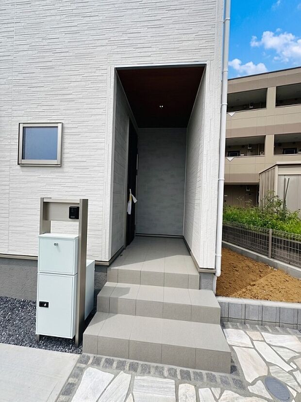 壁に囲まれるように設けられた玄関まわりは、雨の日にも落ち着いて出入りしやすい設計。L字型のアプローチが外からの視線を遮りやすく、プライバシーにも配慮された玄関スペースです。
