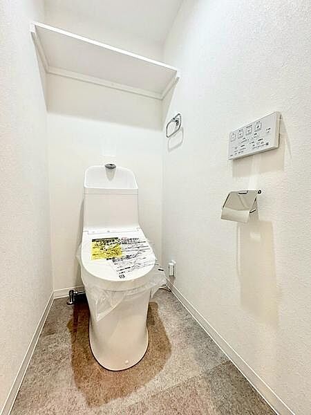 清潔感を意識した設計のトイレです。壁付け収納で空間を有効活用しているほか、温水洗浄機能付きパネルを装備。床材にはお手入れしやすい素材を採用しています。