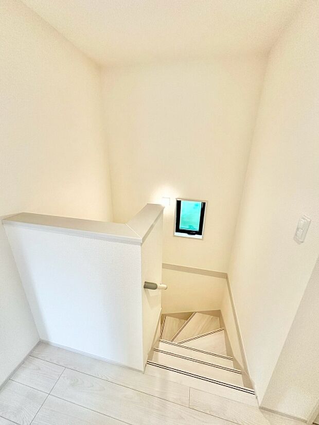 採光窓から自然光が差し込む明るい階段。手すり付きで昇り降りしやすく、白い壁と木目が調和したすっきりとした空間です。