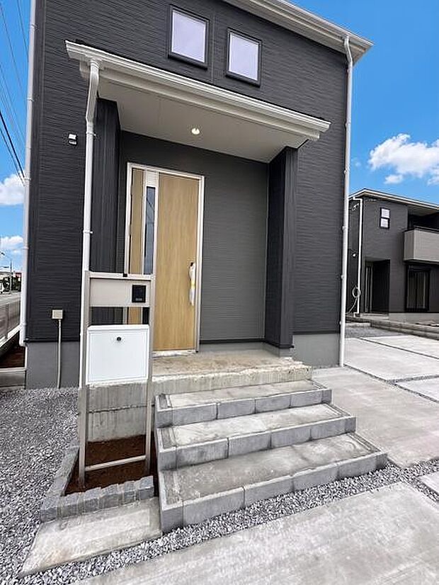 ダークカラーの外壁と木目調の玄関ドアが印象的です。シンプルなデザインで合わせやすい外観です。アプローチのステップもすっきりと仕上がっています。郵便ポストも設置されており機能面にも配慮されています。
