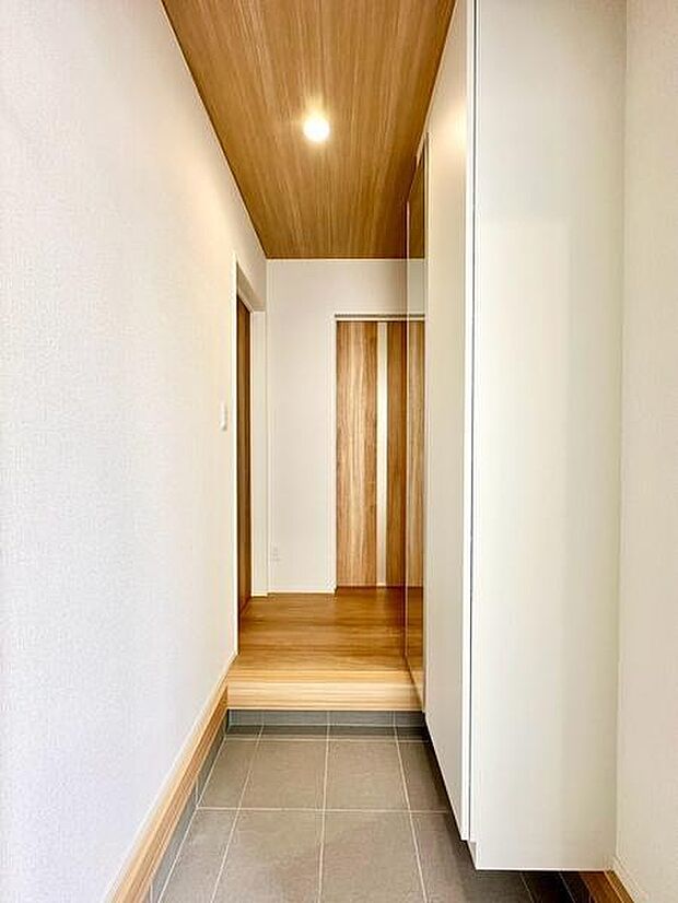 木目調の床や天井、扉が目を引く温かみのある玄関。グレーのタイルを採用した土間が空間を引き締め、落ち着いた雰囲気を演出します。