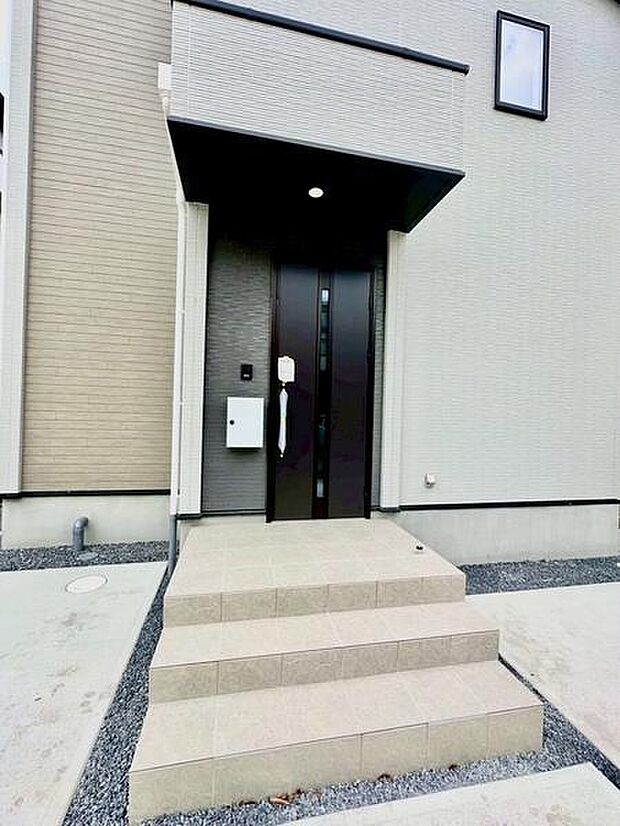 白を基調とした外観に黒の玄関が上品さを与えます。雨除けの庇があり安心感があります。階段も広めでゆとりを感じます。