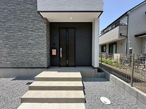 スタイリッシュな外観が印象的な玄関です。ブラックの扉とタイルステップが落ち着いた雰囲気を演出しています。屋根付きのエントランスは雨の日も安心です。玄関周りがすっきりとしたデザインになっています。