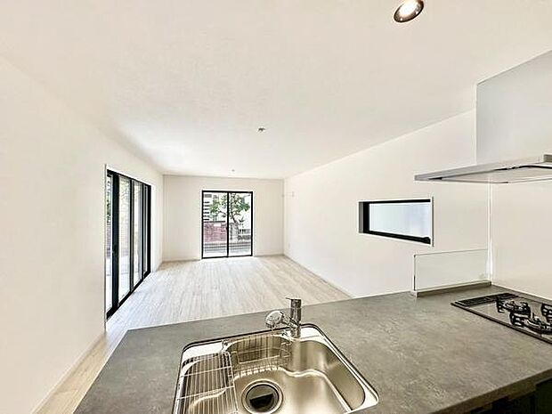 リビングは大きな窓から光が差し込み明るい雰囲気です。白を基調とした内装が空間を広く感じさせます。キッチンからリビング全体を見渡せる造りです。床材も落ち着いた色合いでまとまっています。