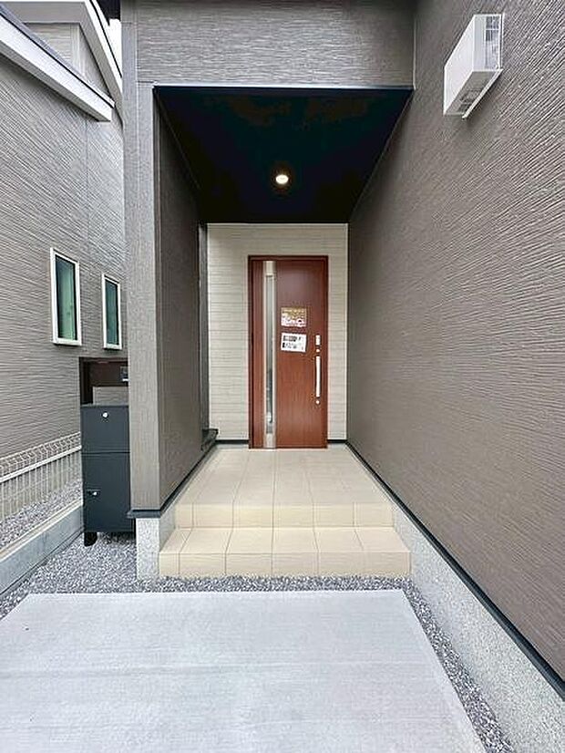 直線的なデザインが際立つシンプルな玄関です。落ち着いた外壁の色合いが特徴で堂々とした印象を与えます。玄関ポーチはゆとりがあり毎日の出入りが快適に行えます。扉は縦のラインがアクセントになっています。