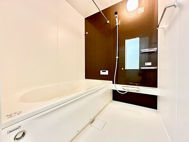 清潔感のあるシンプルなバス空間が広がっています。浴室全体が明るくまとめられ壁面のアクセントカラーが特徴的です。手すりや鏡などの設備も備わっており使いやすさが感じられます。