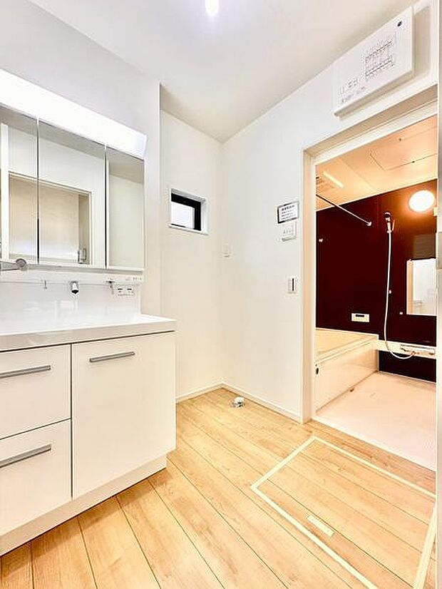明るい空間が特徴の洗面台・洗面所です。収納付きの鏡扉が整理整頓をサポートします。隣接するバスルームへの動線も便利です。床材の木目デザインがやさしい印象を与えます。
