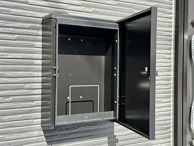 無機質なデザインの宅配ボックスが設置されています。外壁と調和するシンプルな形状です。暗証番号ダイヤル付きで安心感があります。メンテナンスもしやすい位置に配置されています。
