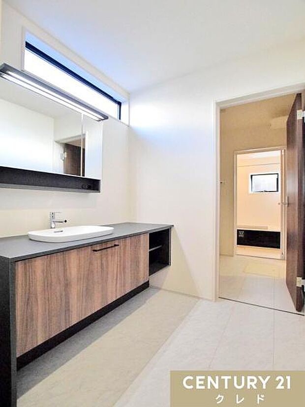 木目調の扉がやさしい雰囲気を演出する、広々とした洗面台。高窓から自然光が差し込み、朝の身支度も気持ちよく始められる空間です。