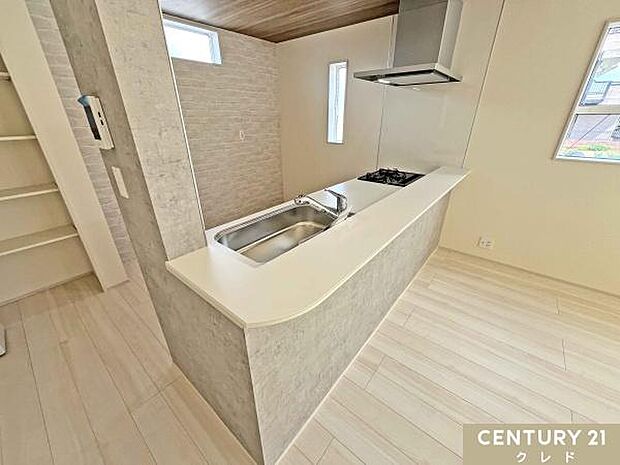 お料理中もリビングの様子が見える、人気の対面式カウンターキッチン。グレーの石目調パネルと背面のレンガ調クロスが、カフェのような洗練された空間を演出します。