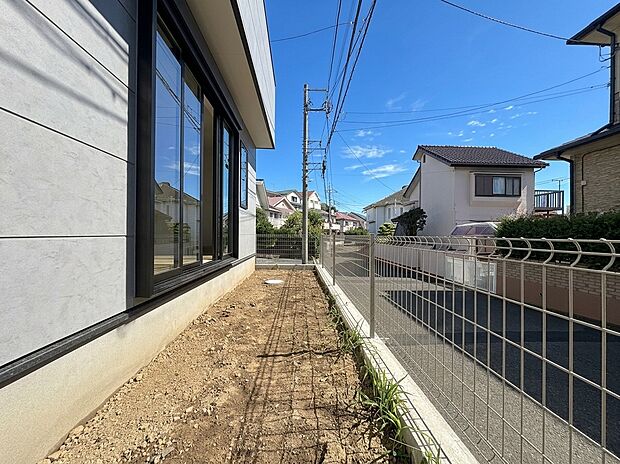 建物脇の通路とフェンス越しの周辺住宅