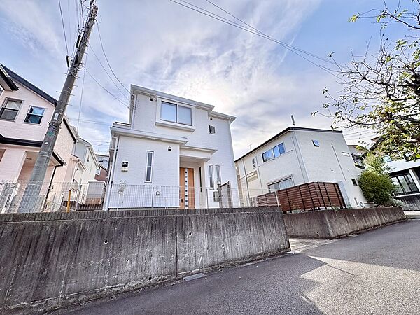 坂道沿いに建つ白い2階建ての住宅外観です
