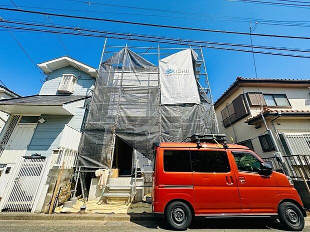 外壁工事中の二階建て住宅の外観と赤い車