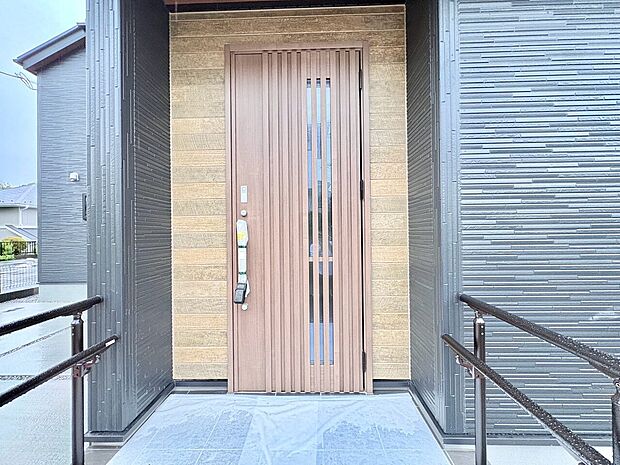 木目調の片開き玄関ドアと手すり付きのスロープ