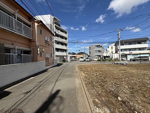前面道路と隣接する更地、周辺に住宅や建物が見える