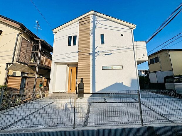 白い外壁の3階建て住宅と門扉、前面道路