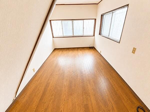 明るい採光が魅力の洋室です。木目調のフローリングが落ち着いた雰囲気を演出します。窓が多く開放感のある空間です。壁面のデザインが個性的な印象を与えます。電源コンセントもしっかり備わっています。