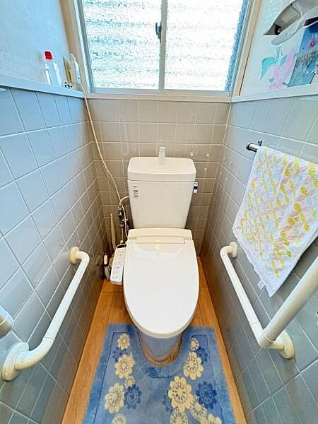窓付きで換気がしやすいトイレです。手すりが両側に設置されており安心して利用できます。清潔感のあるタイル壁が特徴です。明るい雰囲気の空間になっています。