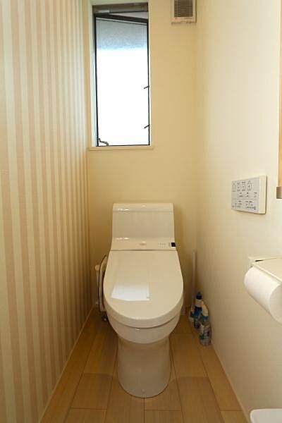 窓が設けられているため換気がしやすく清潔感のあるトイレです。壁の一部にストライプのデザインが採用され空間にアクセントが加わっています。温水洗浄便座が設置されており操作パネルも分かりやすい配置です。
