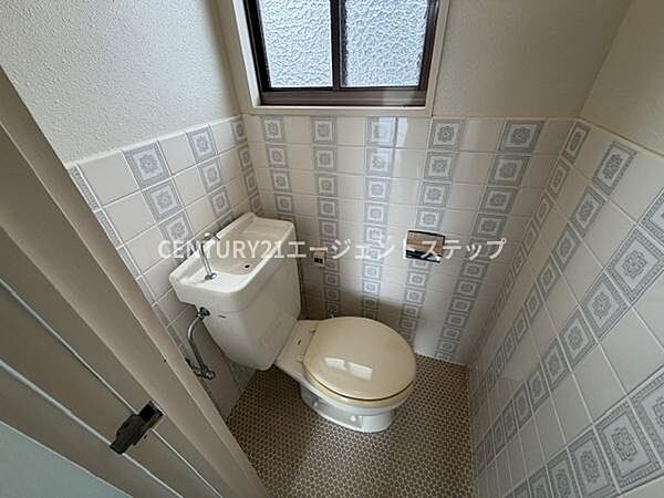明るい窓付きのトイレスペースです。壁のタイルデザインが特徴的で清潔感があります。換気がしやすい構造となっています。コンパクトながらも必要な設備が整っています。