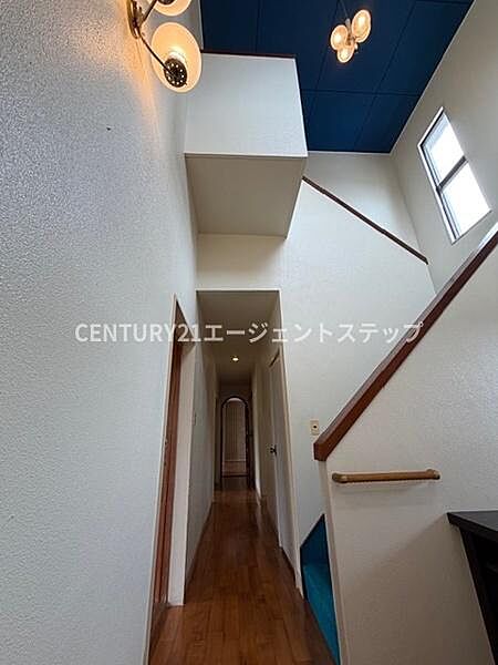 階段と廊下が直線的に配置され空間の広がりを感じられる造りです。壁の淡い色調と木目の床材が落ち着いた雰囲気を演出しています。窓からの自然光が廊下を明るく照らします。