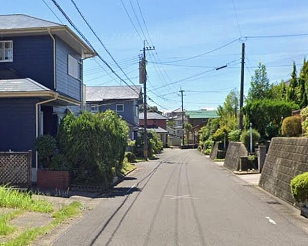 前面道路はフラットで歩行や車の通行もスムーズです。周囲の植栽や住宅が整然と並び落ち着いた雰囲気が感じられます。幅員がしっかり確保された道路沿いの現地写真です。