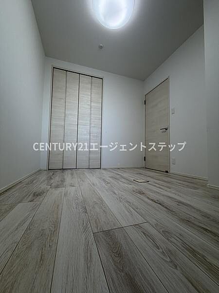 明るい色合いのフローリングが広がる洋室です。クローゼットも備わっており収納に便利です。天井の照明が空間をしっかり照らします。シンプルな内装で使いやすいお部屋です。ドアやクロゼットも統一感があります。