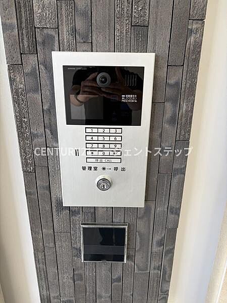 シンプルなデザインのインターホンが設置されています。視認性の高いボタン配置が特徴的です。建物の雰囲気に調和したパネルが魅力となっています。セキュリティ面にも配慮された仕様です。