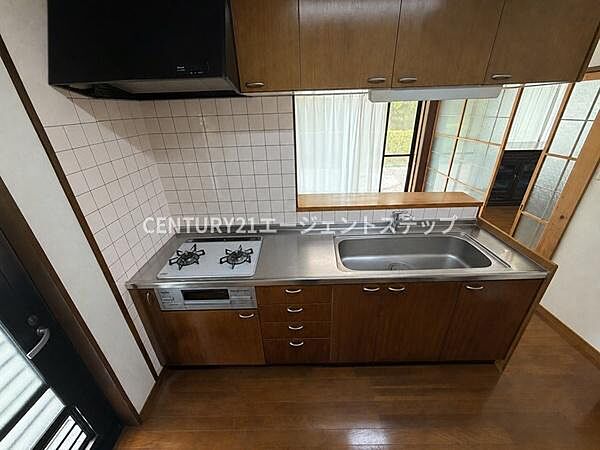 収納スペースが豊富なキッチンです。シンプルなデザインで清潔感があります。ガスコンロと換気扇が備え付けられています。広々とした作業スペースが確保されています。床材と木目調の扉が統一感を演出しています。