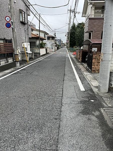 前面道路は舗装されており幅員も十分に確保されています。周辺には電柱や街路樹が整然と配置されすっきりとした印象です。静かな住宅街の雰囲気が感じられる現地写真です。
