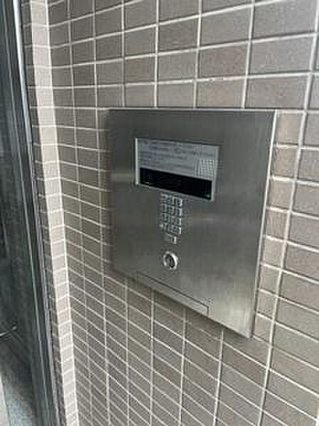 エントランスにはスタイリッシュな操作パネルが設置されております。無駄のないデザインが空間に調和しています。タイル貼りの壁面が印象的です。金属の質感がアクセントとなっております。