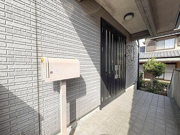 玄関には屋根があり天候に左右されにくい設計です。タイル張りのアプローチが清潔感を感じさせます。ポストも設置されており便利な仕様となっています。広めのスペースがゆとりを感じさせる玄関エリアです。