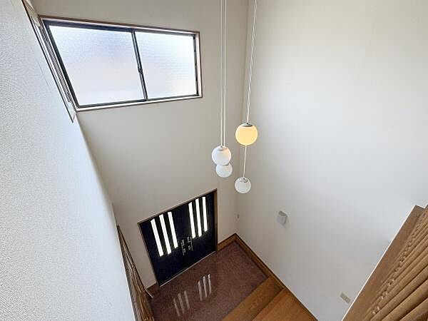 玄関吹き抜けの開放感が印象的です。上下階に明かりを取り入れる窓があり明るさが感じられます。モダンな照明が空間を引き立てています。落ち着いた色合いの玄関ドアがアクセントです。