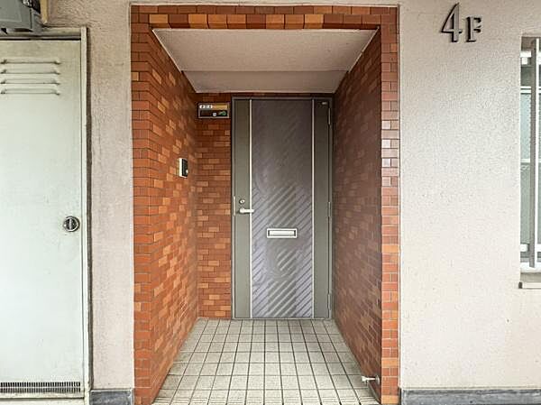 レンガ調の壁が印象的な玄関です。シンプルな玄関ドアが設置されています。天井には照明もあり夜間の出入りも安心です。広めのタイル敷きスペースが確保されています。