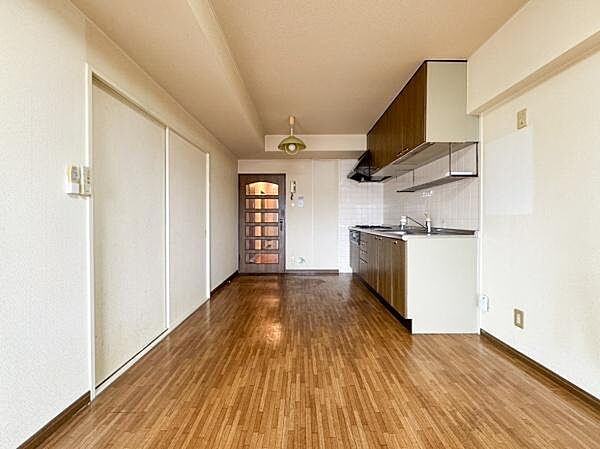 キッチンとリビングが一体となった開放感のある空間です。木目調のフローリングが温かみを演出しています。壁付けキッチンでお部屋がすっきりと使えます。収納スペースも豊富に確保されています。
