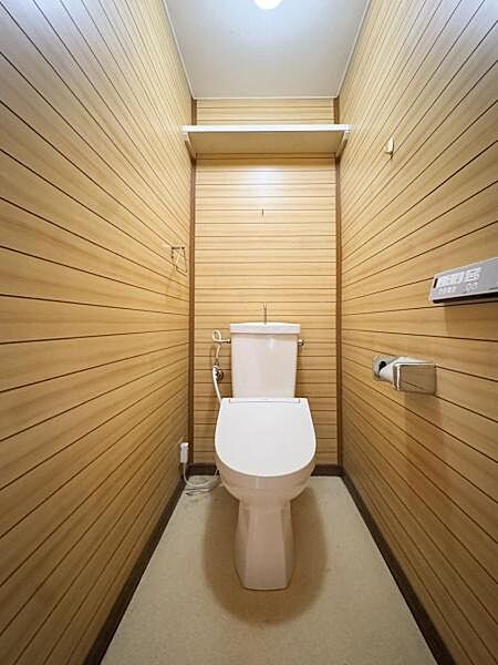 木目調の壁面が特徴的なトイレです。室内はシンプルで手入れがしやすい空間。上部には便利な棚が設置されています。照明の明るさも十分に感じられる仕様です。