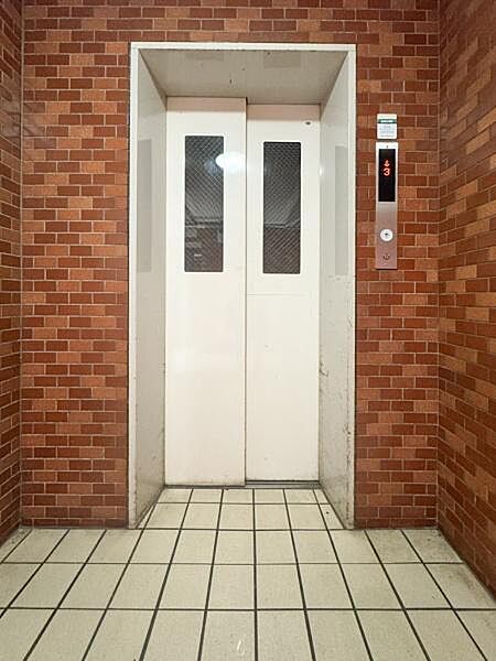 レンガ調の壁が印象的なエレベーターです。シンプルなデザインで周囲と調和しています。ボタン操作盤も見やすい位置に設置されています。共用部として利用しやすい空間が広がっています。